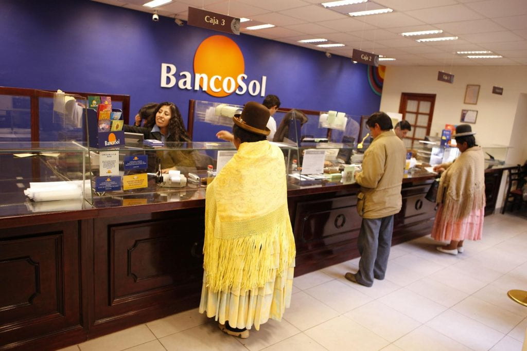 Photo of interior of the El Alto branch of BancoSol, with cuistomers in traditional and indigenous attire transacting bank business with tellers.