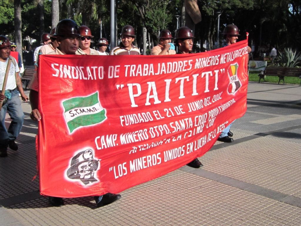 A photo of miners protesting, carrying a banner through the streets in Santa Cruz.