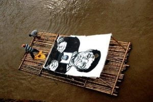 Photo of the artist Gabriel Posada, on a raft in the Cauca River with Vinyl paint images of the disappeared in 