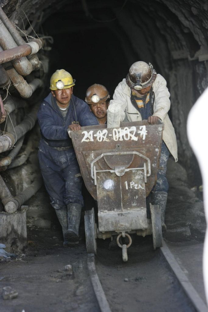 A photo of three miners pushing a railcart out of a mine.