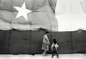 A woman and two young children walk before an enormous Chilean flag.
