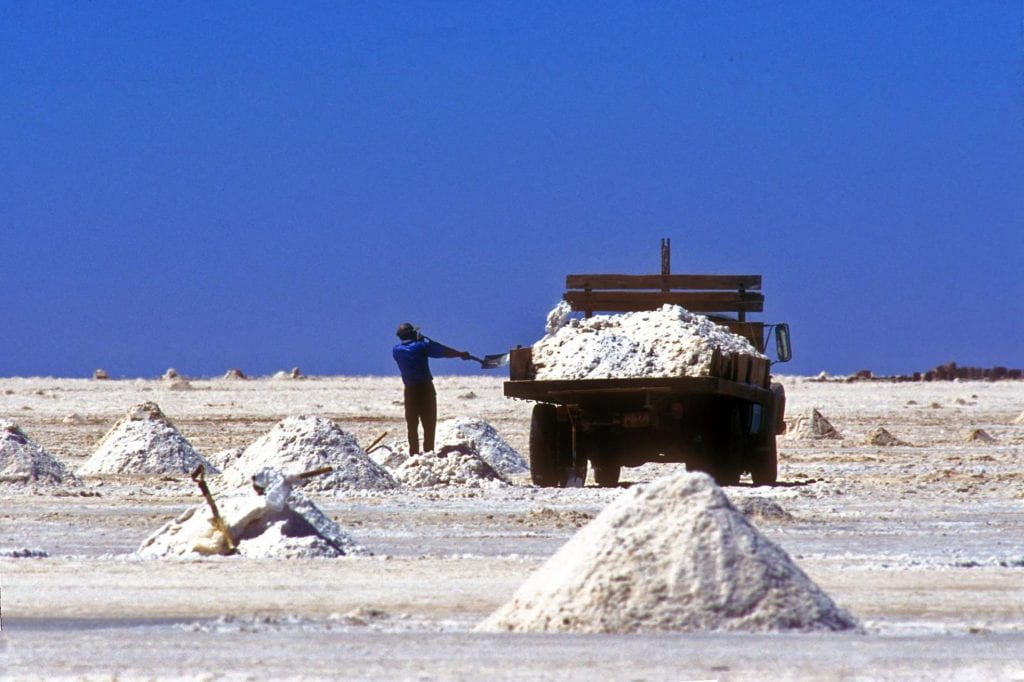 Photo of a salt mine in Salar de Uyuni, showing piles of salt, as well as a man shoveling salt into a truck.