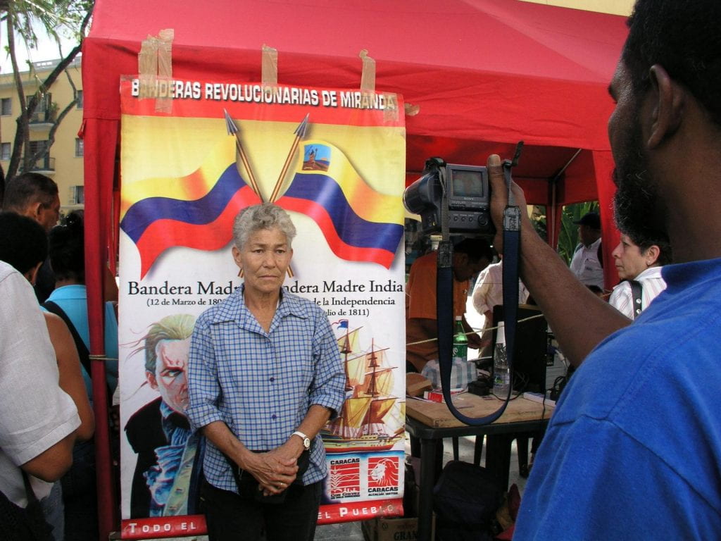 A woman in a blue shirt gets her photograph taken for her Bolivarian ID card for subsidies.