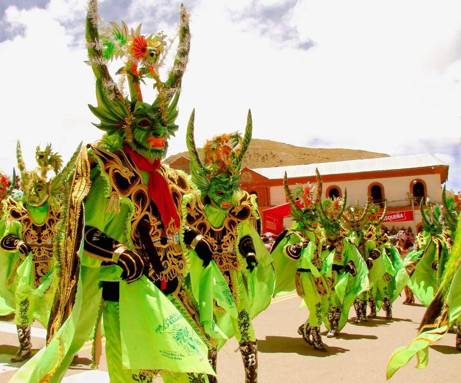 Images of the dancing devils, diablos dan- zantes, in Puno, Peru. A large group of dancers, with lime green and black costumes, and very long horns on their heads, represent the devils in the dance.