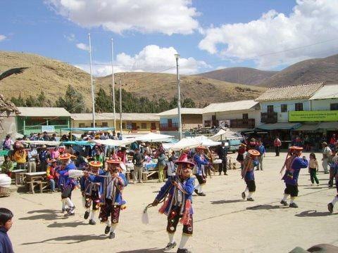 A festival in honor of the señor de Qoyllur rit’i in the Peruvian highlands., with dancers in traditional attire dancing in a square, with an open market and houses in the background.