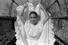 Photo of a Colombian girl in East Boston, 2003. She is wearing a traditional white dress for dancing. Her hands are above her head.