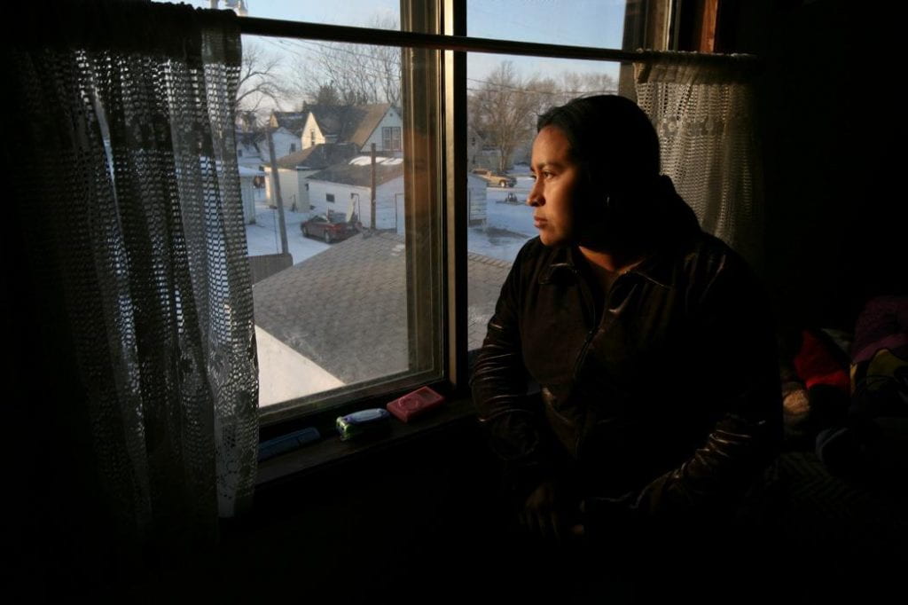 Rosario Toj, a worker under house arrest, looks out the window at an Iowa winter's day. She was saving up money to buy her father in Guatemala a new prosthetic foot when she was caught in the raid.