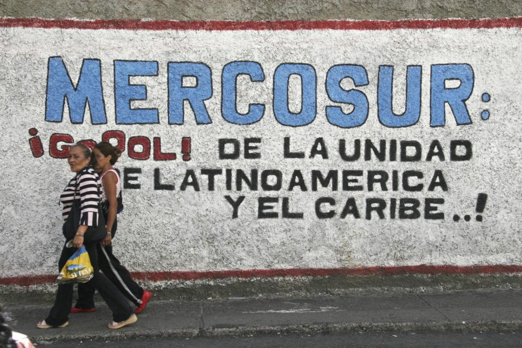People walk past a wall mural praising Mercosur, a Common Market of the South.