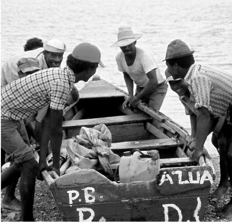 Five men in short-sleeve shirts, shorts, and hats launch a small dory boat in the Dominican Republic.