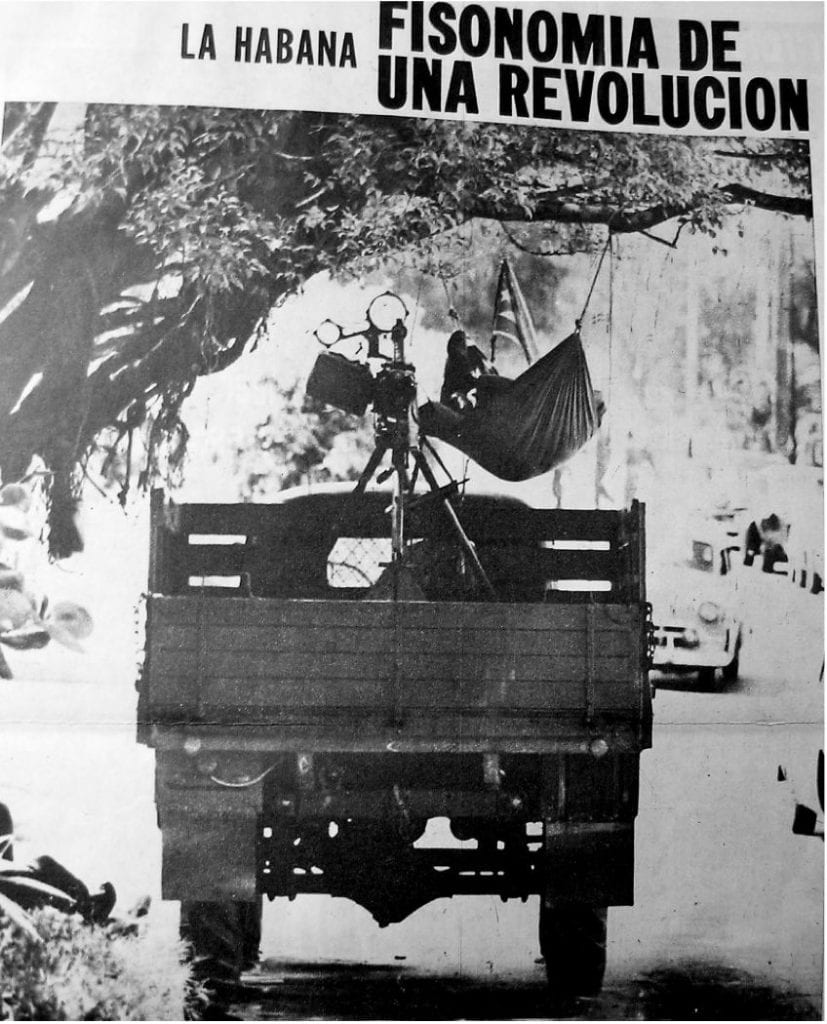 A truck is parked under a tree, a man lays in a hammock. A sign above reads (in Spanish) “Havana: Physiognomy of a Revolution.”