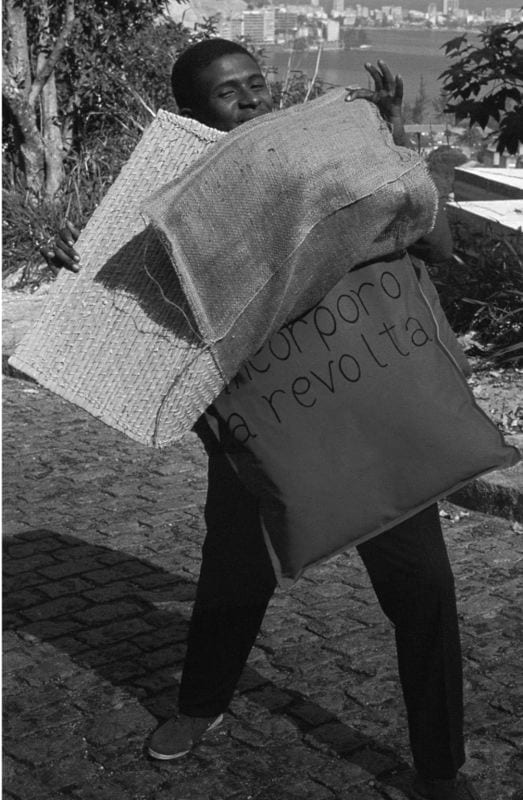Photo of Nildo da Mangueira, wearing a Parangolé (protest sign) with the inscription read: Incorporo a Revolta (I Incorporate Revolt), which could be revolt against the lack of social mobility or against the authoritarian rule imposed by the military dictatorship. It implied a state of aggression as well as a wish for transgression.